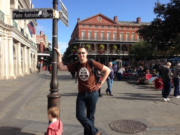 Man leaning on street post with square and lovely buildings behind him in French Quarter New Orleans